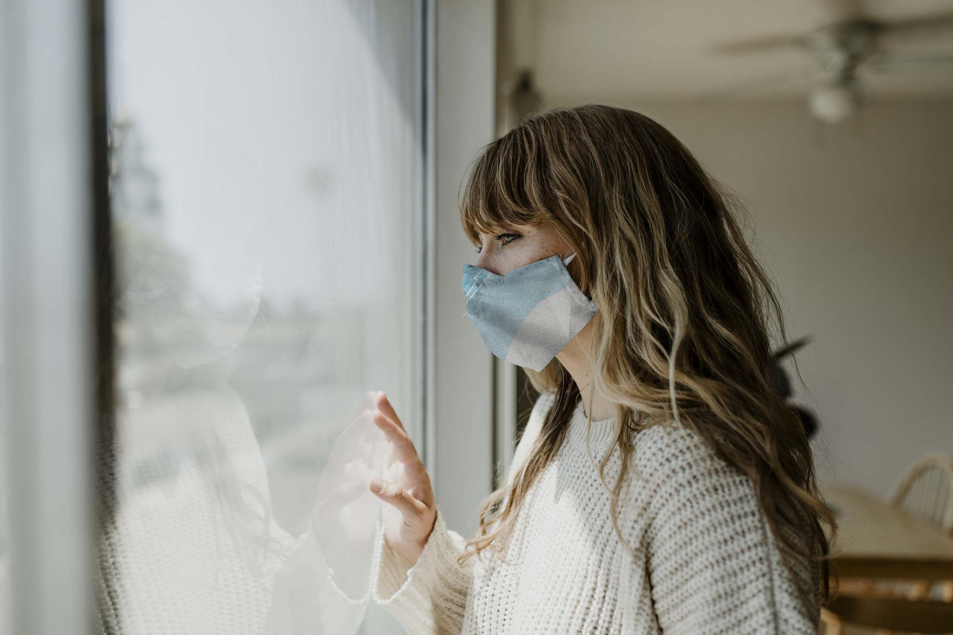 Woman wearing a mask staring out the window during a lockdown